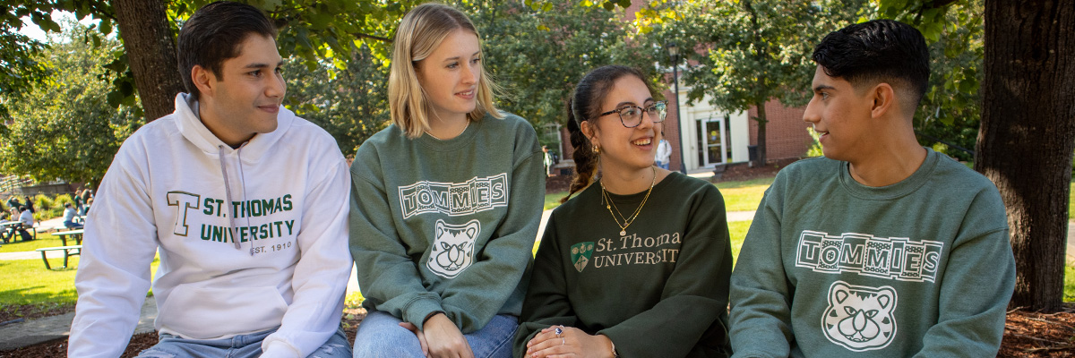 A photo of four students sitting on a ledge on campus in the fall.